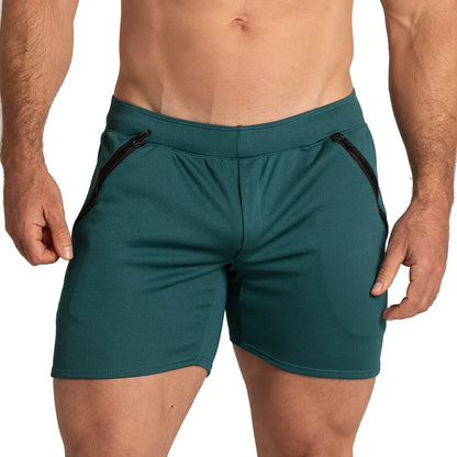 Adult male model wearing green Gigo men’s shorts with zip pocket details, showing front fit, waistband, fabric texture and athletic short length for movement and warm weather.